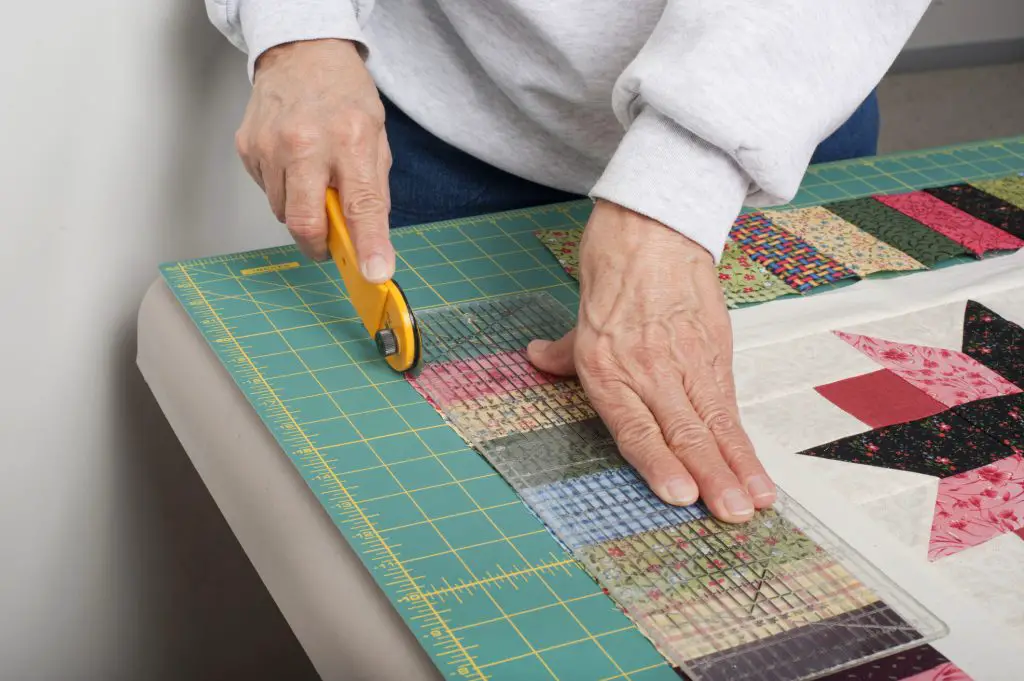 quilter cutting a quilt with a rotary cutter and cutting mat